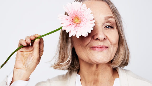 Magazinbild Anti-Aging Ältere Frau hält sich eine Blume vor ein Auge
