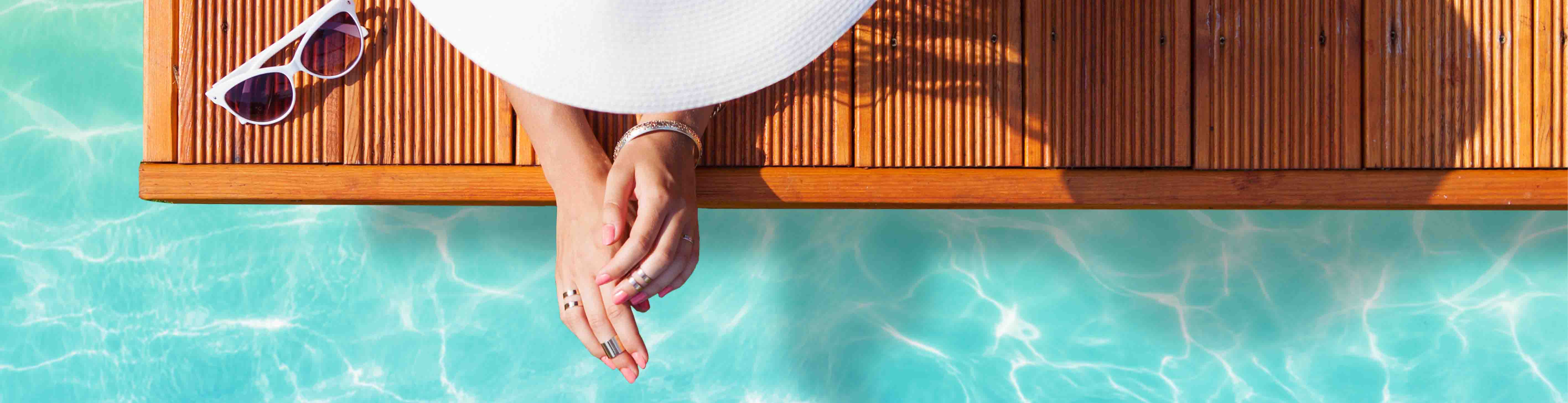 Hurra der Sommer ist da: die richtige Hautpflege im Sommer Frau mit Sonnenhut schaut ins Wasser