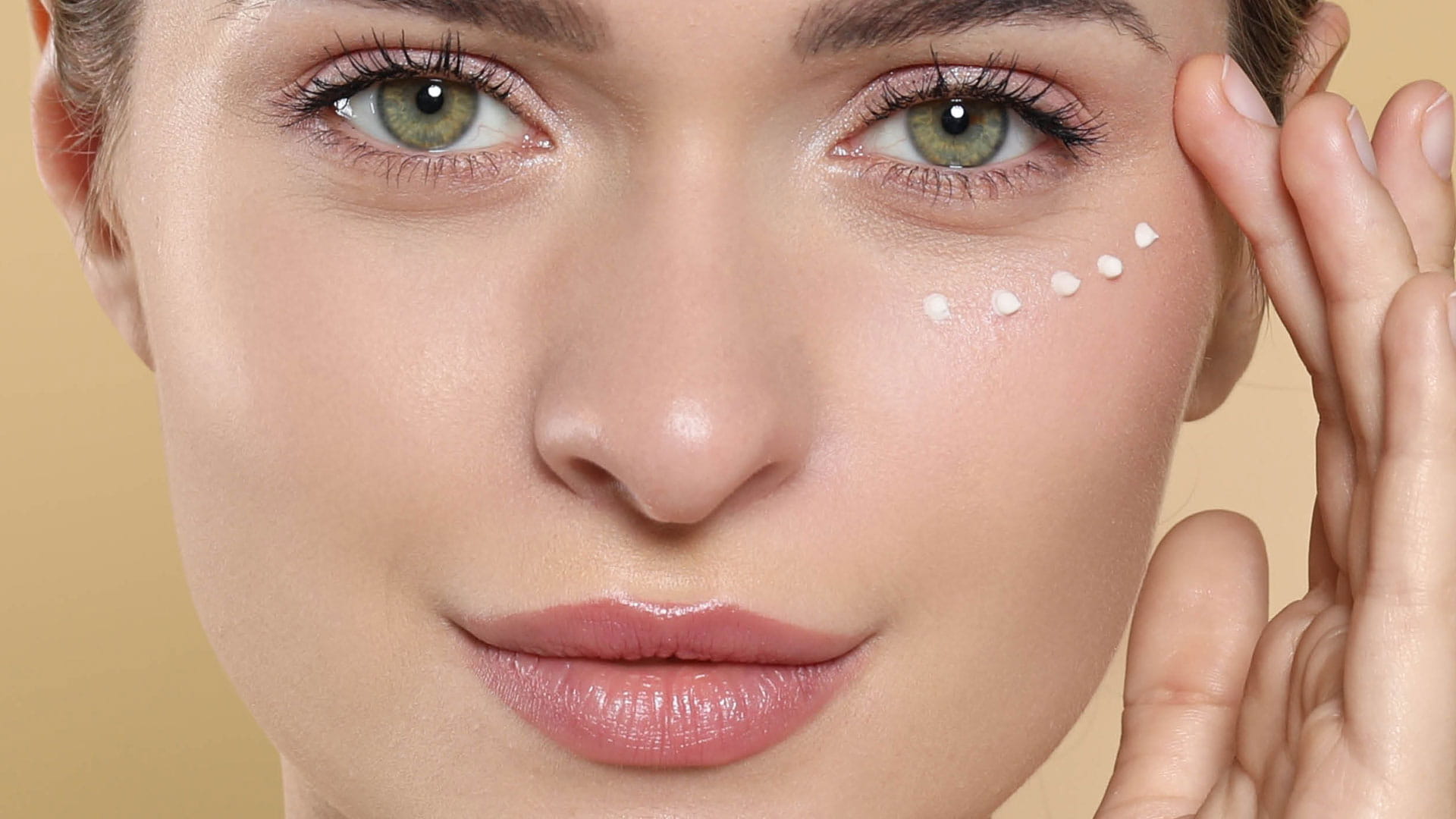 Header Augenpflege Produktgruppe Eine Frau hat sich Tupfen von Augencreme unter dem Auge aufgetragen